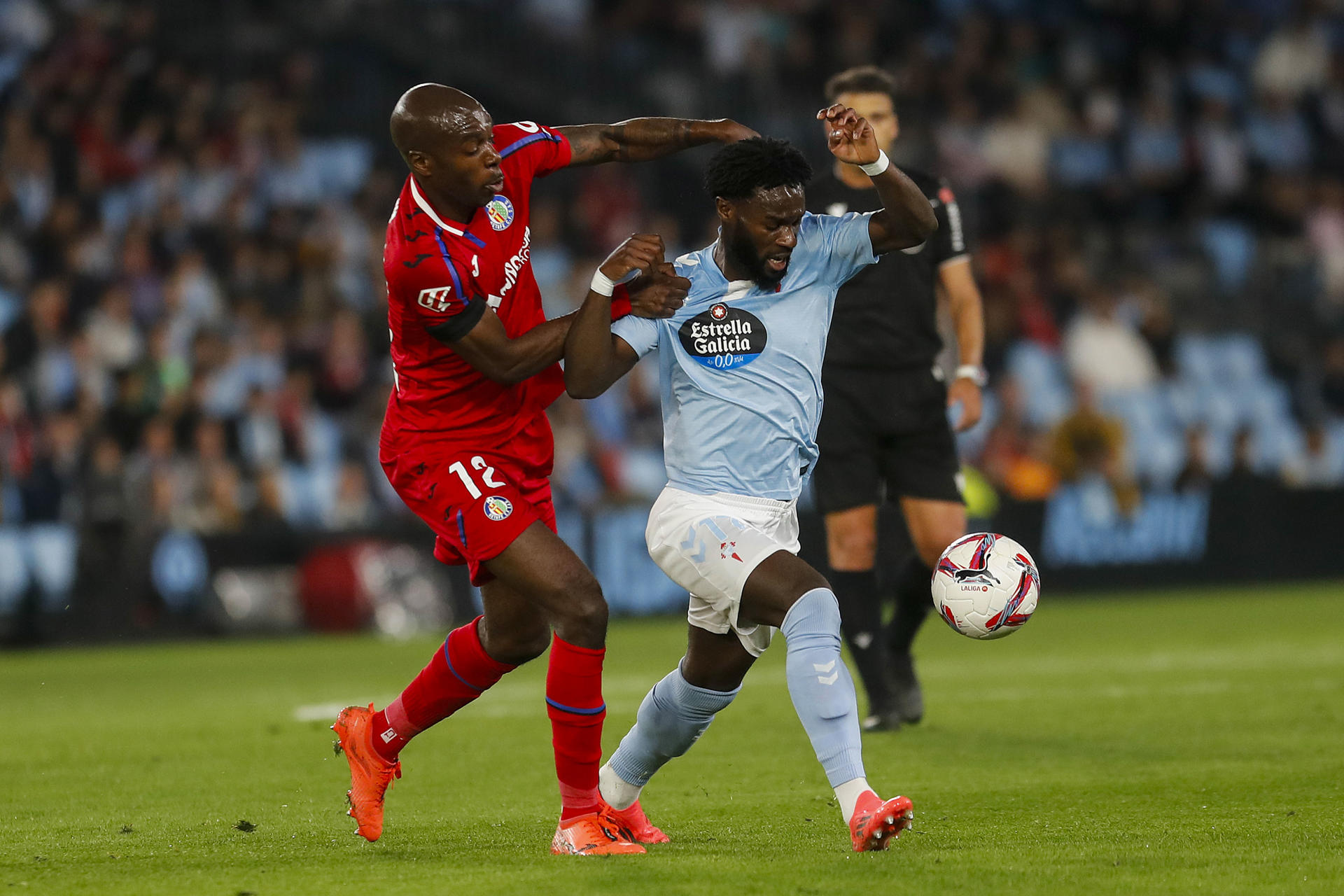 El delantero costamarfileño del Celta, Jonathan Bamba (d), disputa el balón ante el defensa camerunés del Getafe, Allan Nyom, durante el encuentro correspondiente a la jornada 12 de Laliga EA Sports que disputan Celta y Getafe hoy lunes en el estadio Balaidos de Vigo. EFE / Salvador Sas.