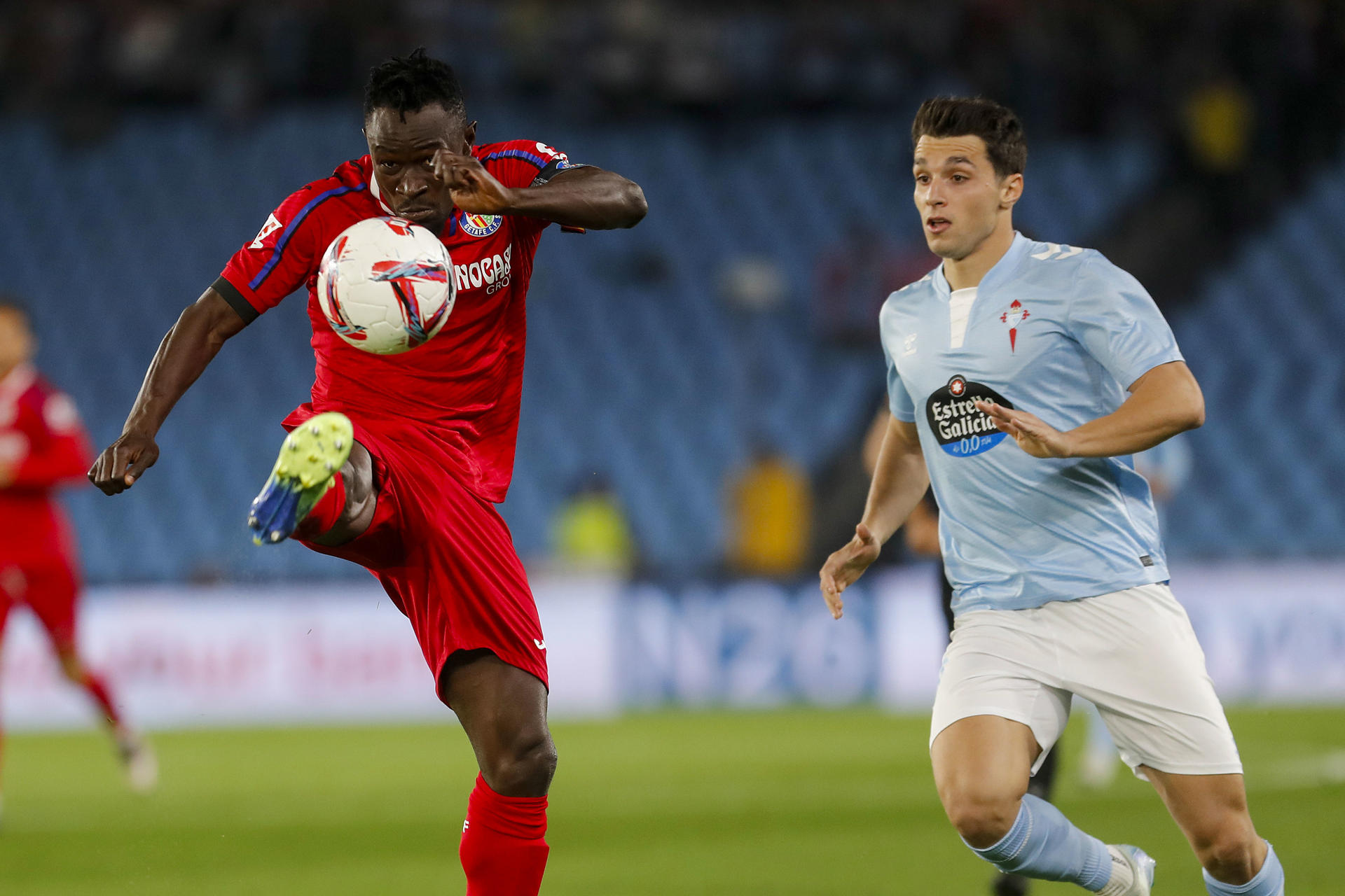El defensa togoleño del Getafe, Djené Dakoman (i), despeja el balón ante el delantero del Celta, Anastasios Douvikas, durante el encuentro correspondiente a la jornada 12 de Laliga EA Sports que disputan Celta y Getafe hoy lunes en el estadio Balaidos de Vigo. EFE / Salvador Sas.